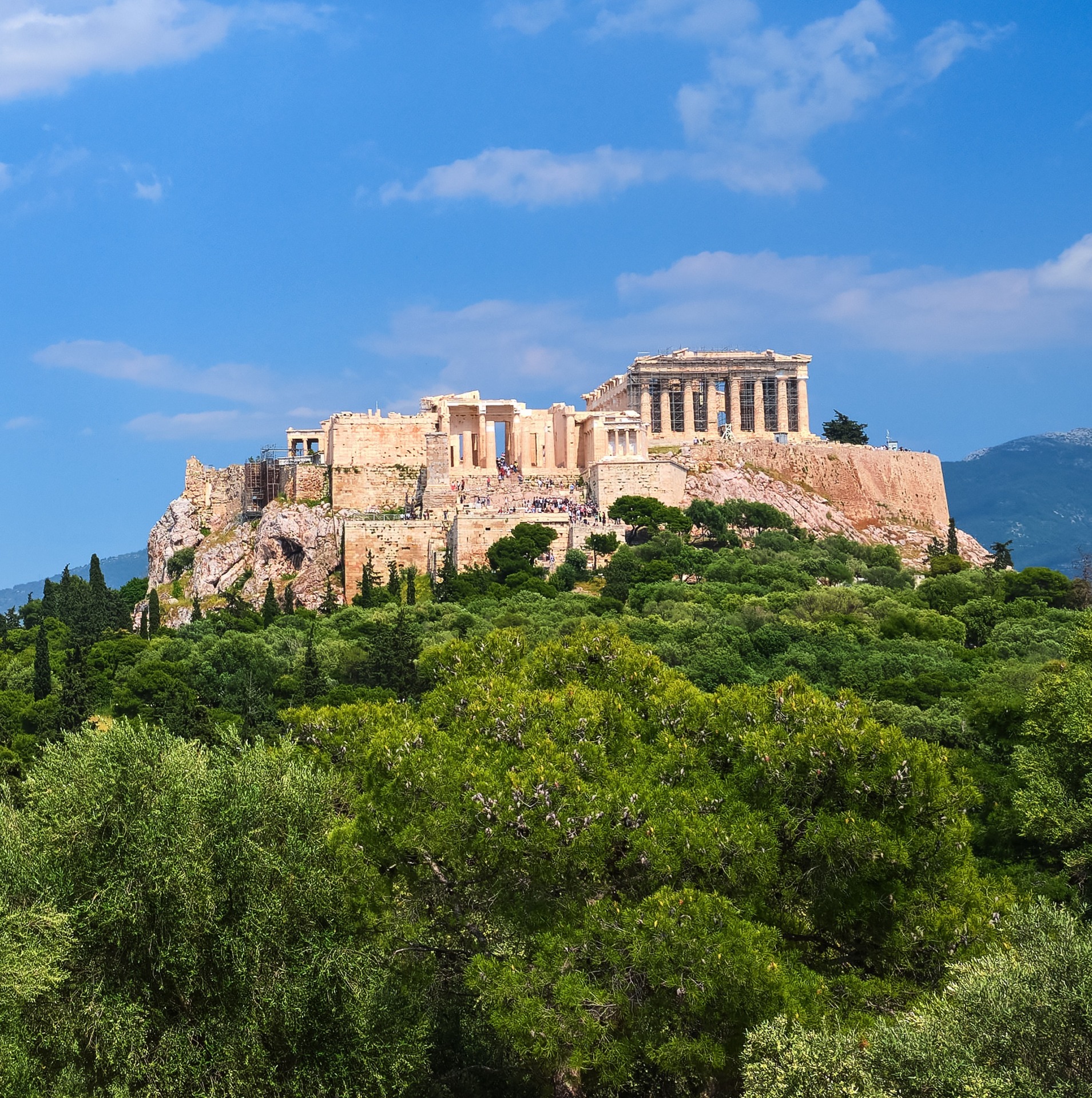 Iconic view of Acropolis hill and Lycabettus hill in background in Athens, Greece from Pnyx hill in summer daylight with great clouds in blue sky.